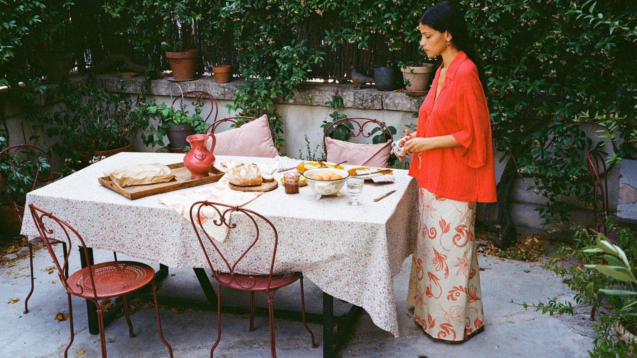 Women standing by outdoor table making lunch wearing a red shirt and printed maxi skirt