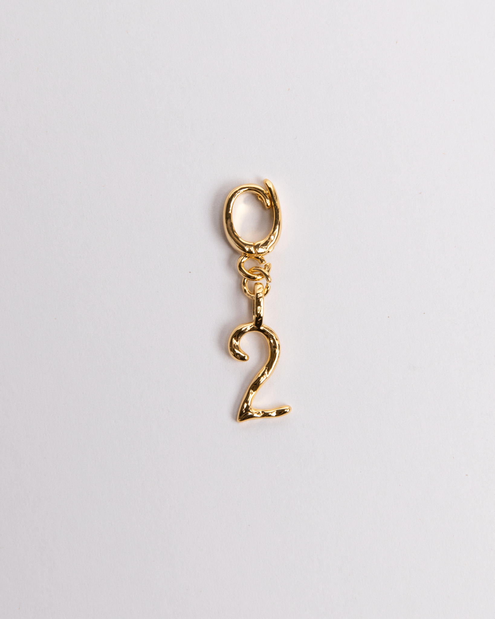 A gold-colored charm in the shape of the number 2 with a secure clasp designed for attaching to jewelry items.