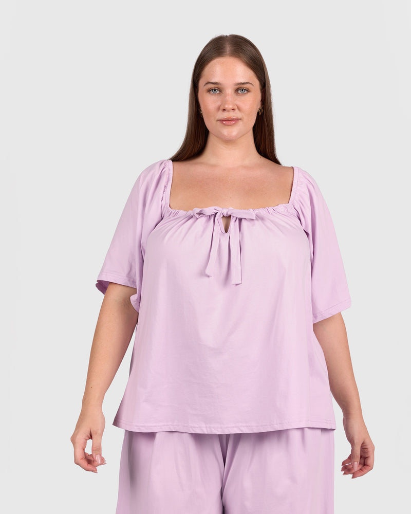 Woman wearing a light purple top and pants on a plain background