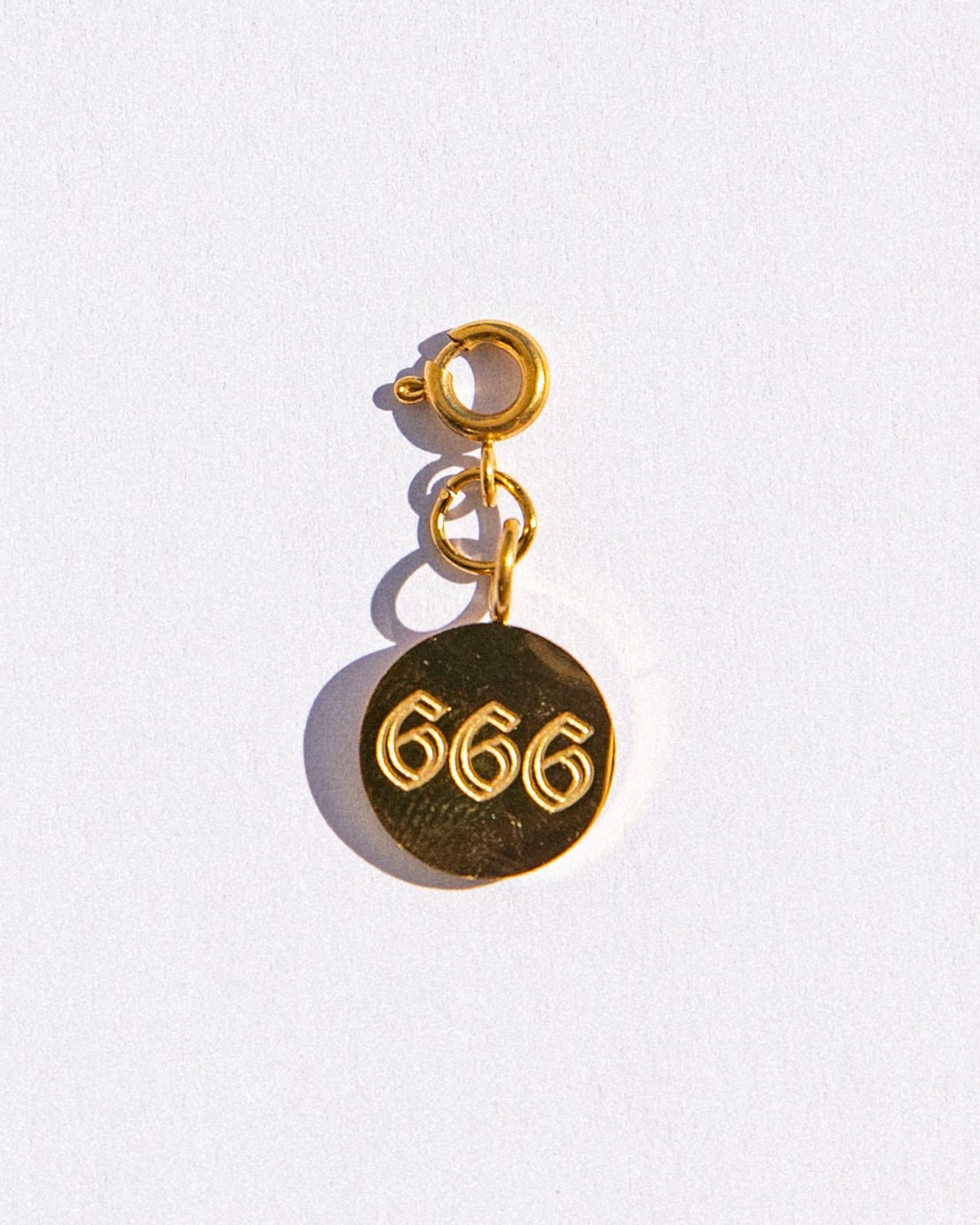 Gold circle charm with angel numbers '666' on a white background