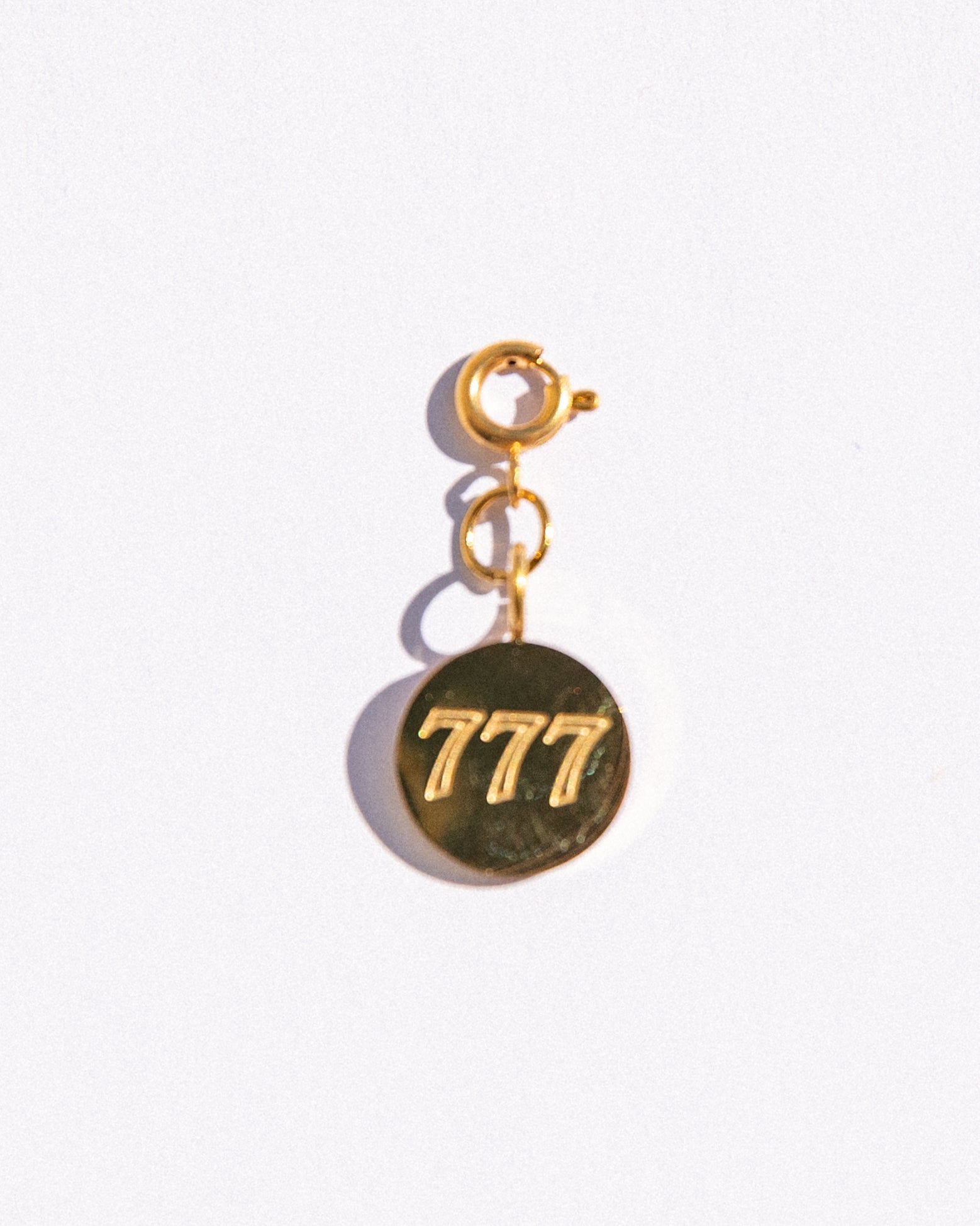 Gold circle charm with angel numbers '777' on a white background