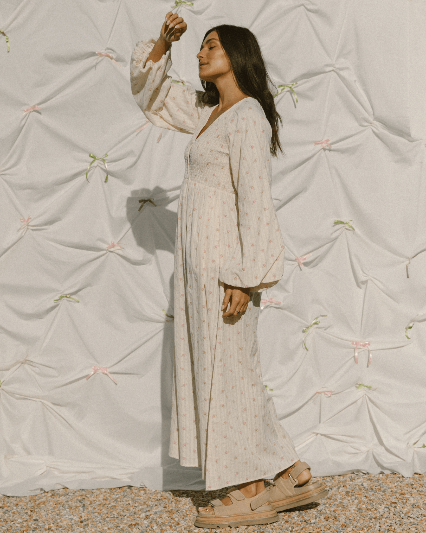 Woman wearing long billowing sleeved dress with a delicate cream & pink flower print.