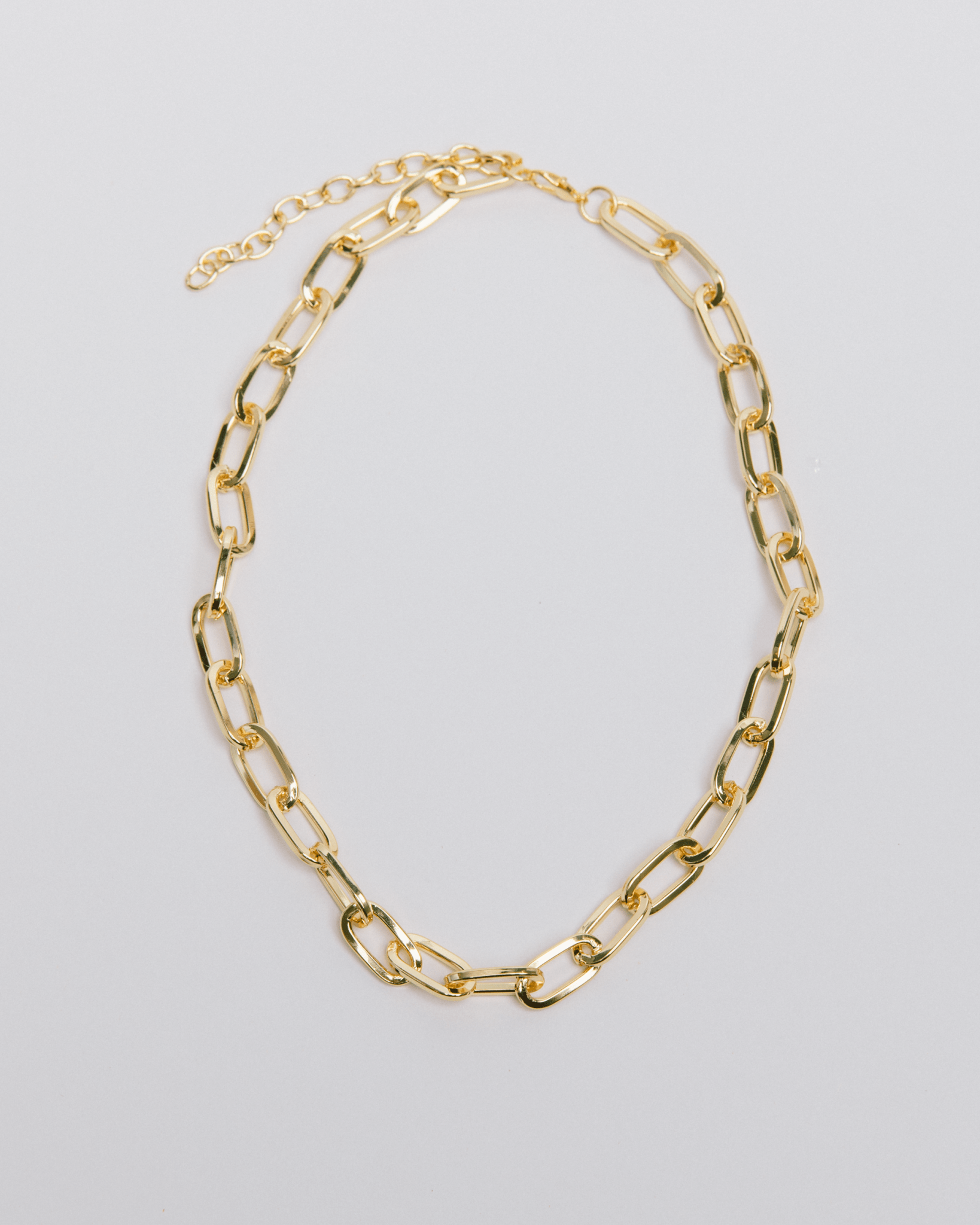 A gold paperclip chain necklace with adjustable length, laid out on a white background.