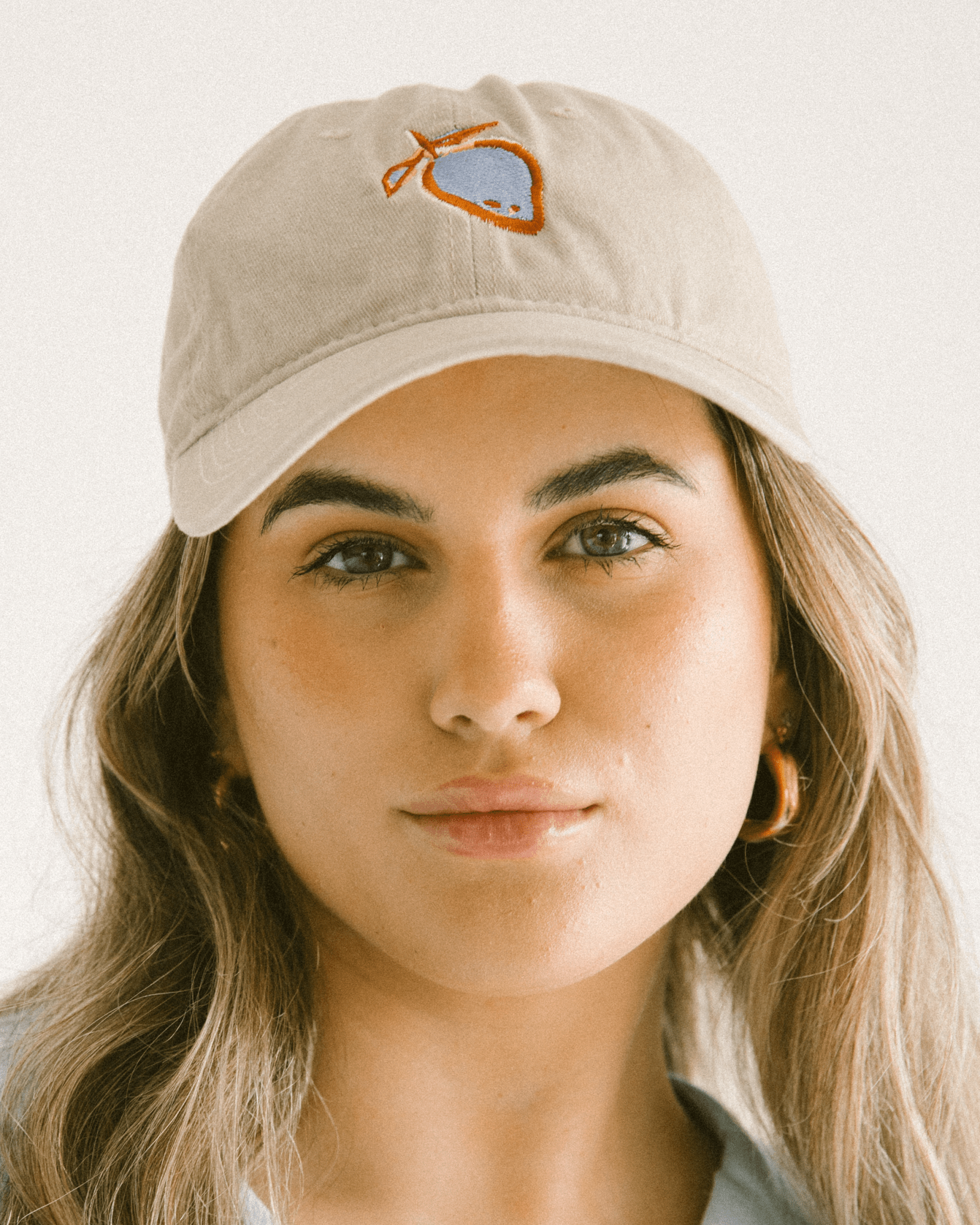 Woman wearing a beige cap with blue & tan fruit embroidered on front.