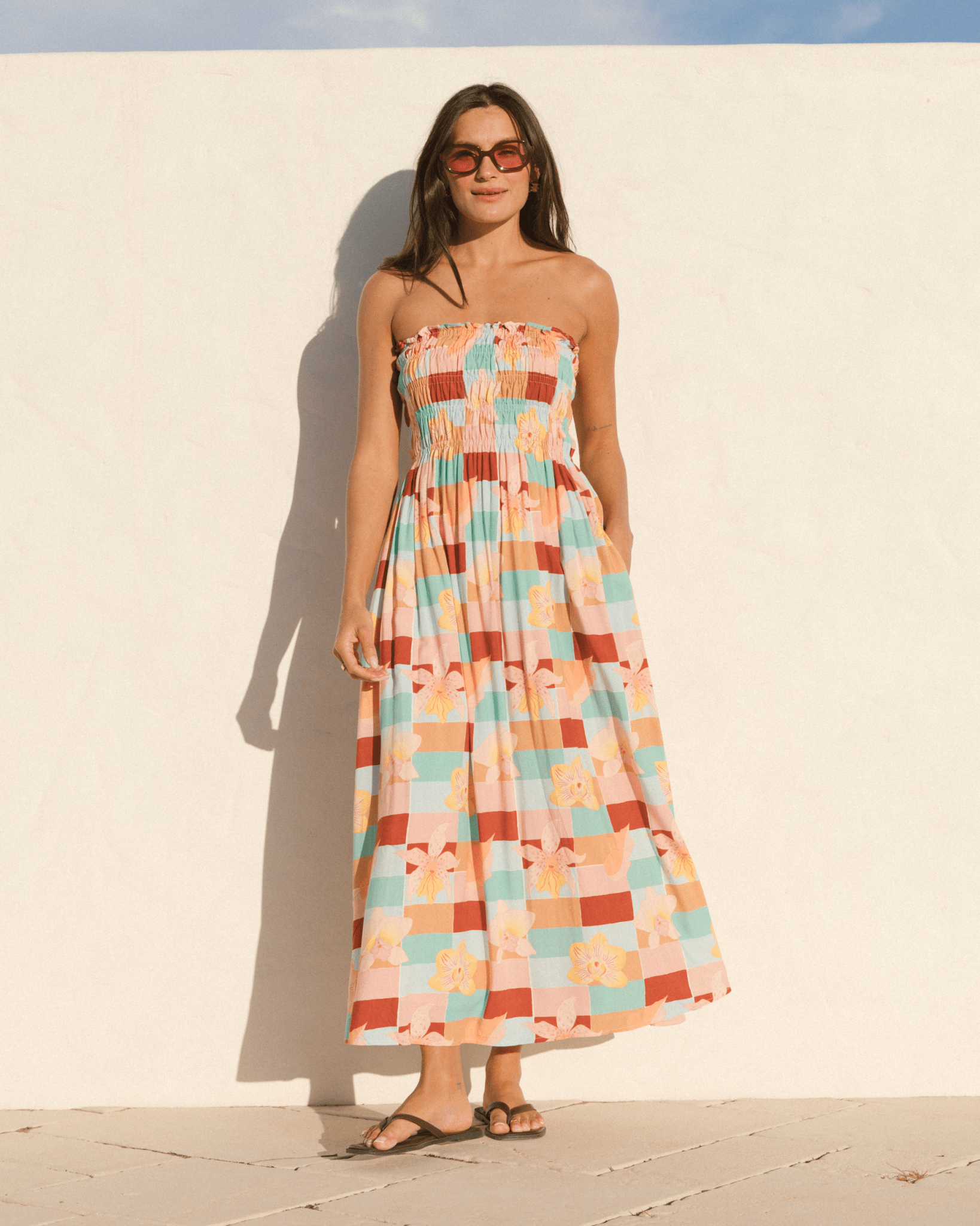 Woman wearing a colorful checkered dress against a white wall.