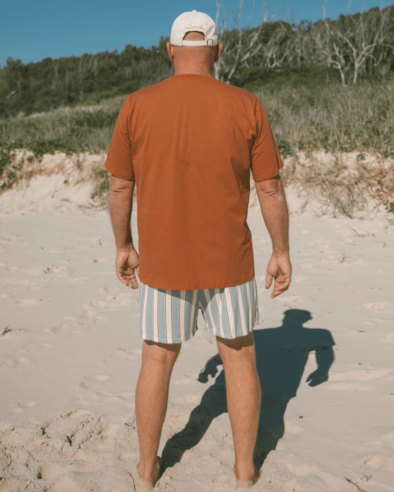 Man walking on a sandy beach wearing an relaxed fit shirt and striped shorts.