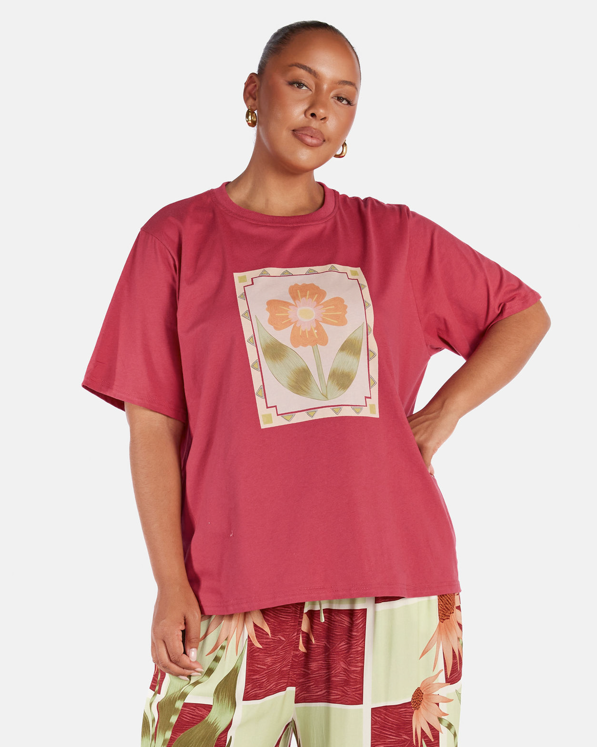 Person wearing a pink t-shirt with a floral design and checkered pants on a white background