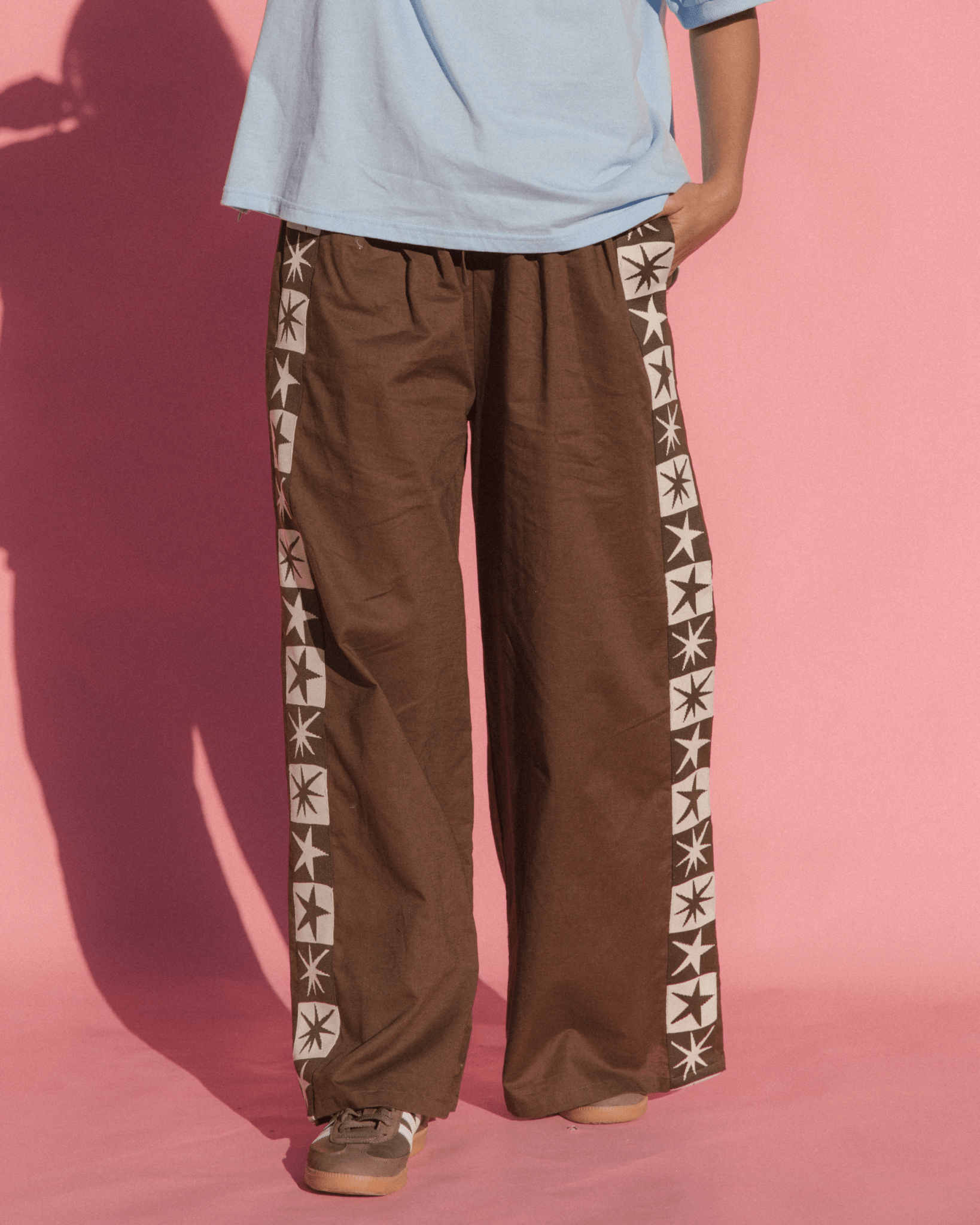 Person wearing brown pants with star patterns on a pink background