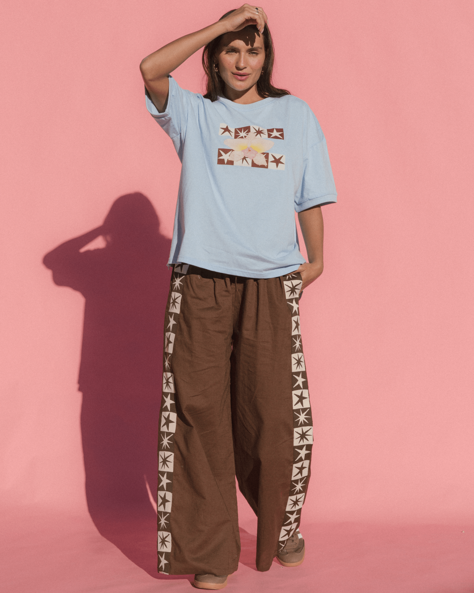 Person wearing a light blue t-shirt with a graphic design and brown pants with star patterns on a pink background
