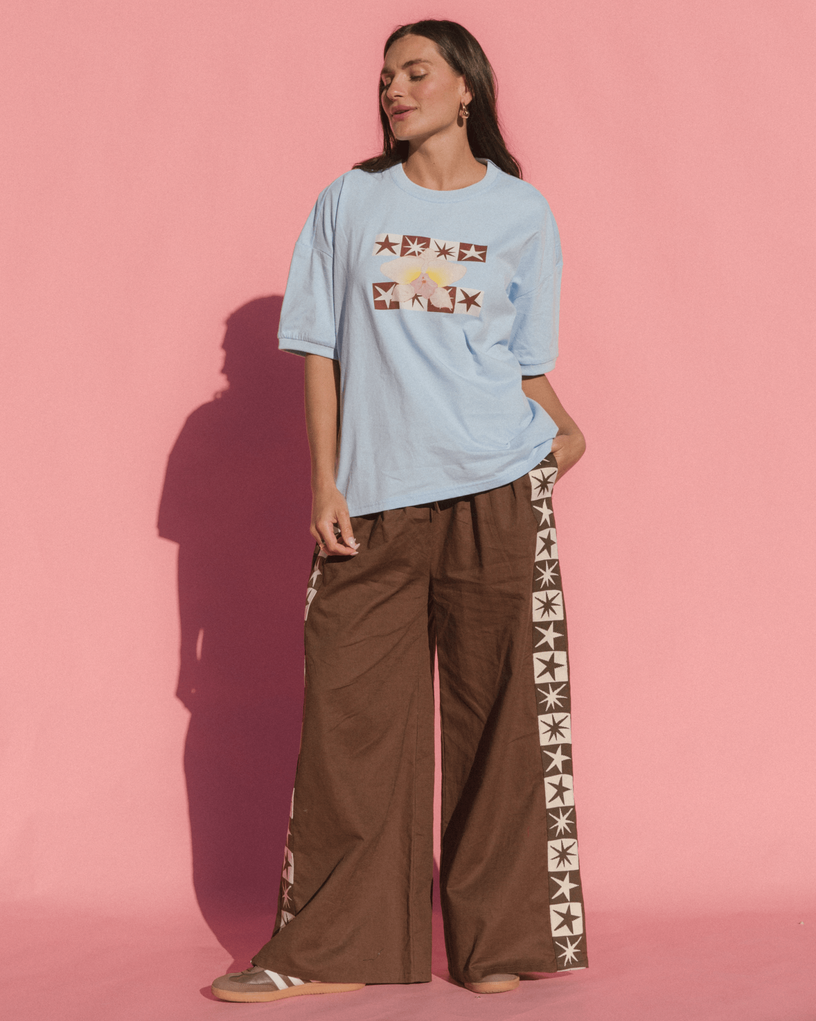 Woman wearing a light blue t-shirt and brown pants with star patterns against a pink background