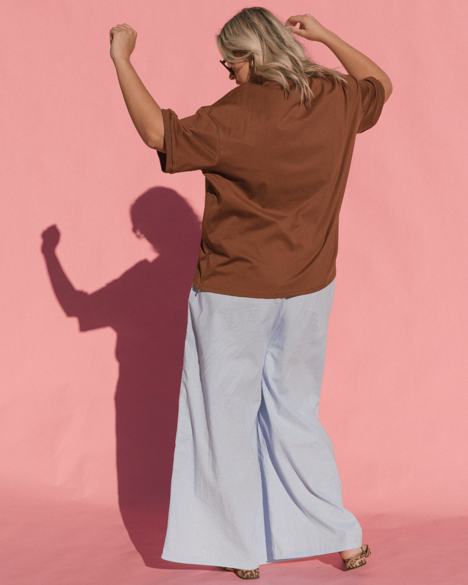 Person wearing a brown shirt and light blue pants against a pink background