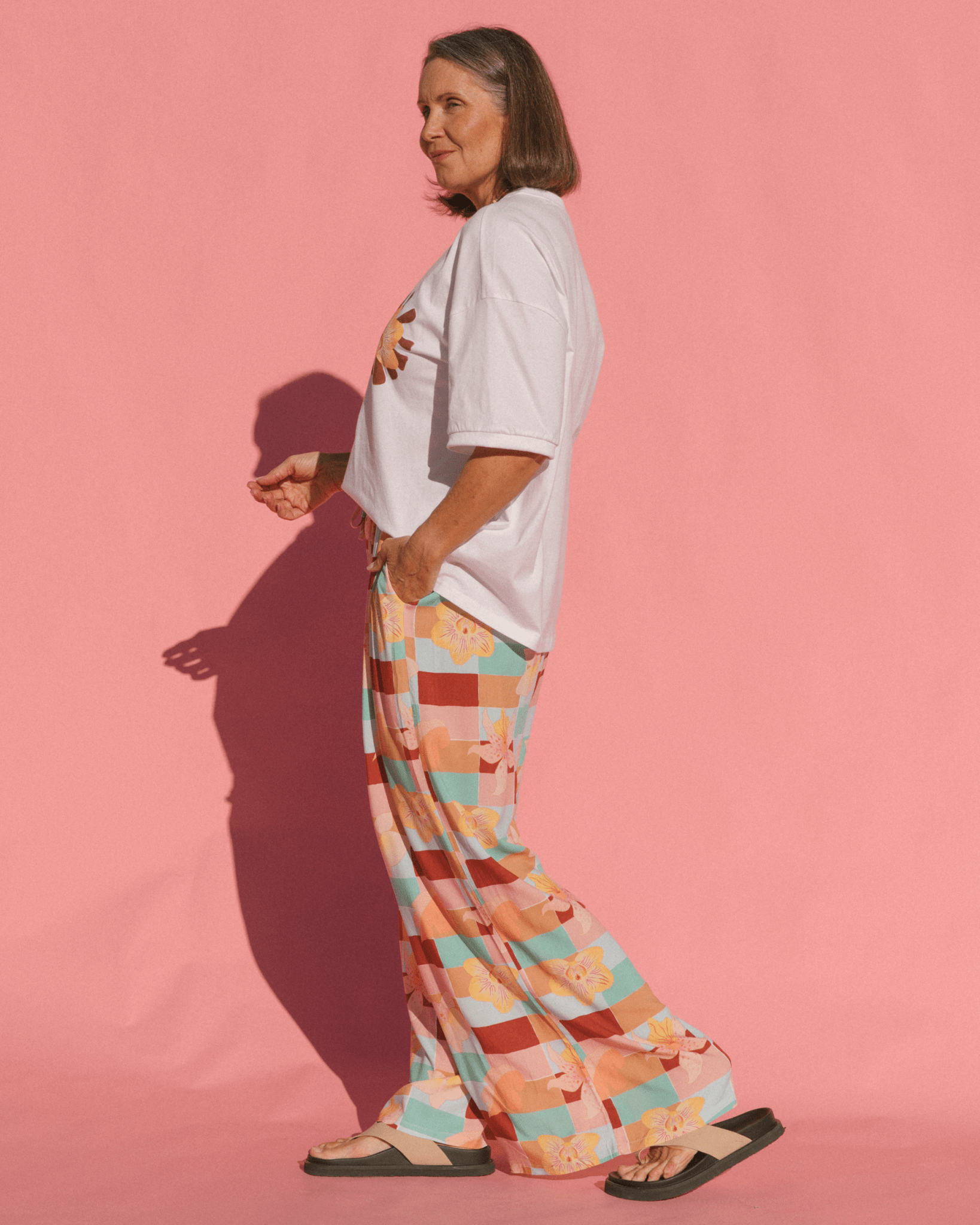 Person wearing a white t-shirt and colorful checkered pants against a pink background