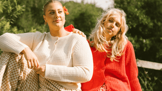 Two women sitting next to each other on a bed outside, wearing printed pyjamas 