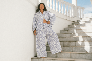 A girl in lounge pants and lounge shirt in blue and white floral print on white stairs blue sky