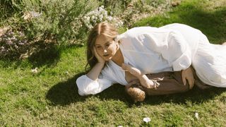 A mother breastfeeding her child laying down in the grass wearing an avalon maxi smock. 