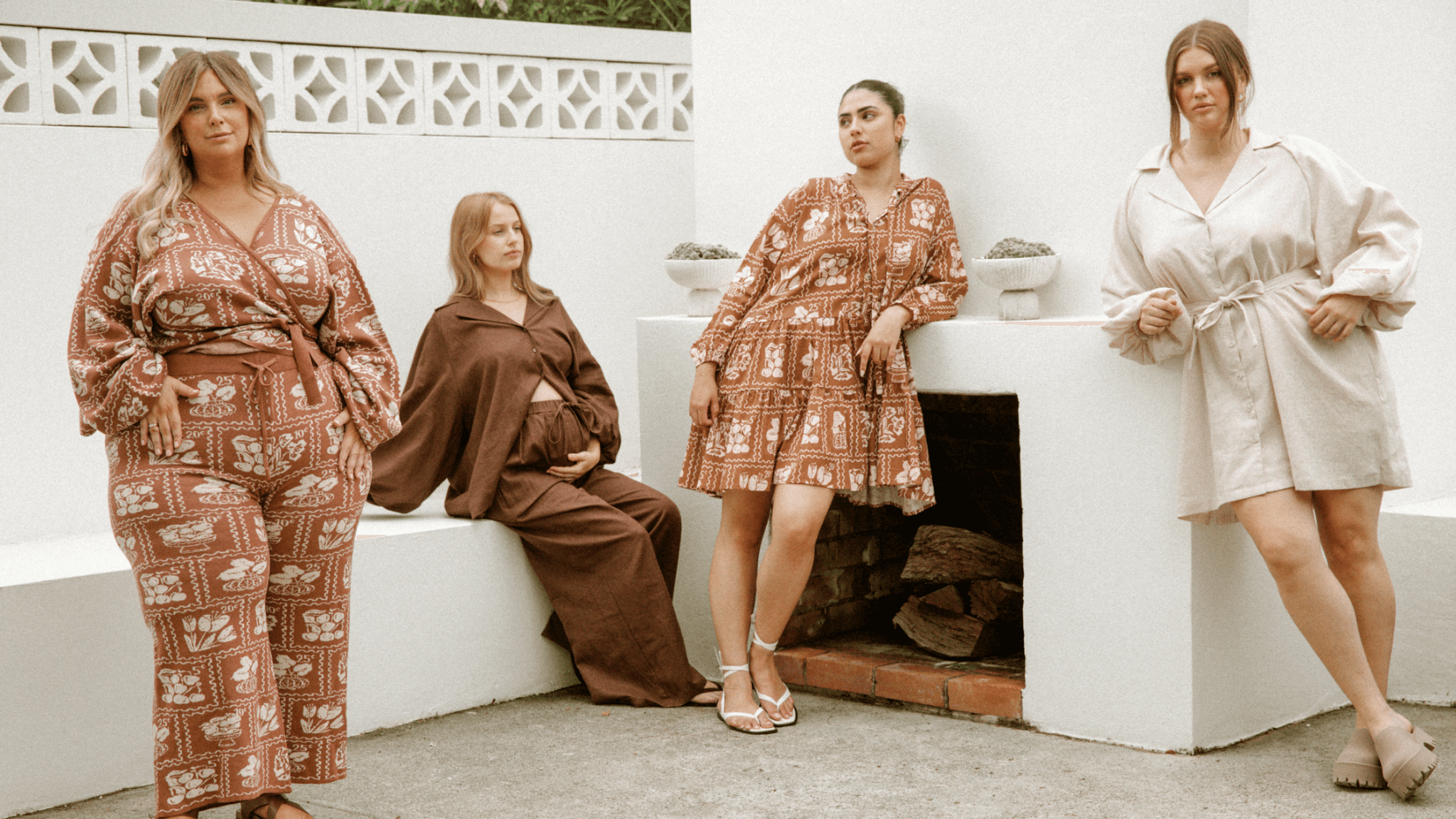 Four women in a backyard area styled in a netural clothing collection in unison, posing and modelling