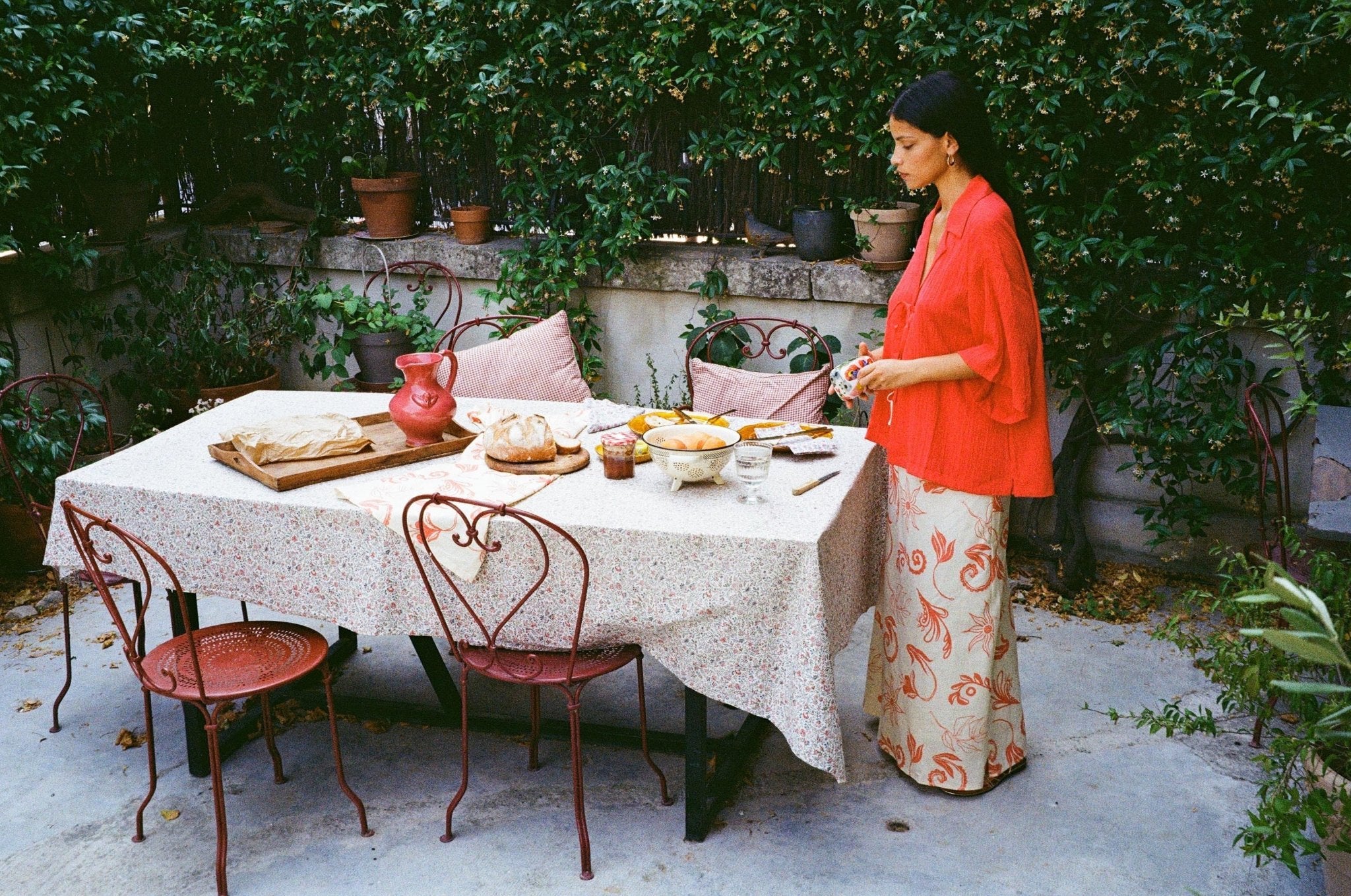 Women standing by outdoor table making lunch wearing a red shirt and printed maxi skirt