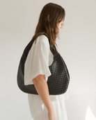 Person wearing a woven black handbag on a plain background