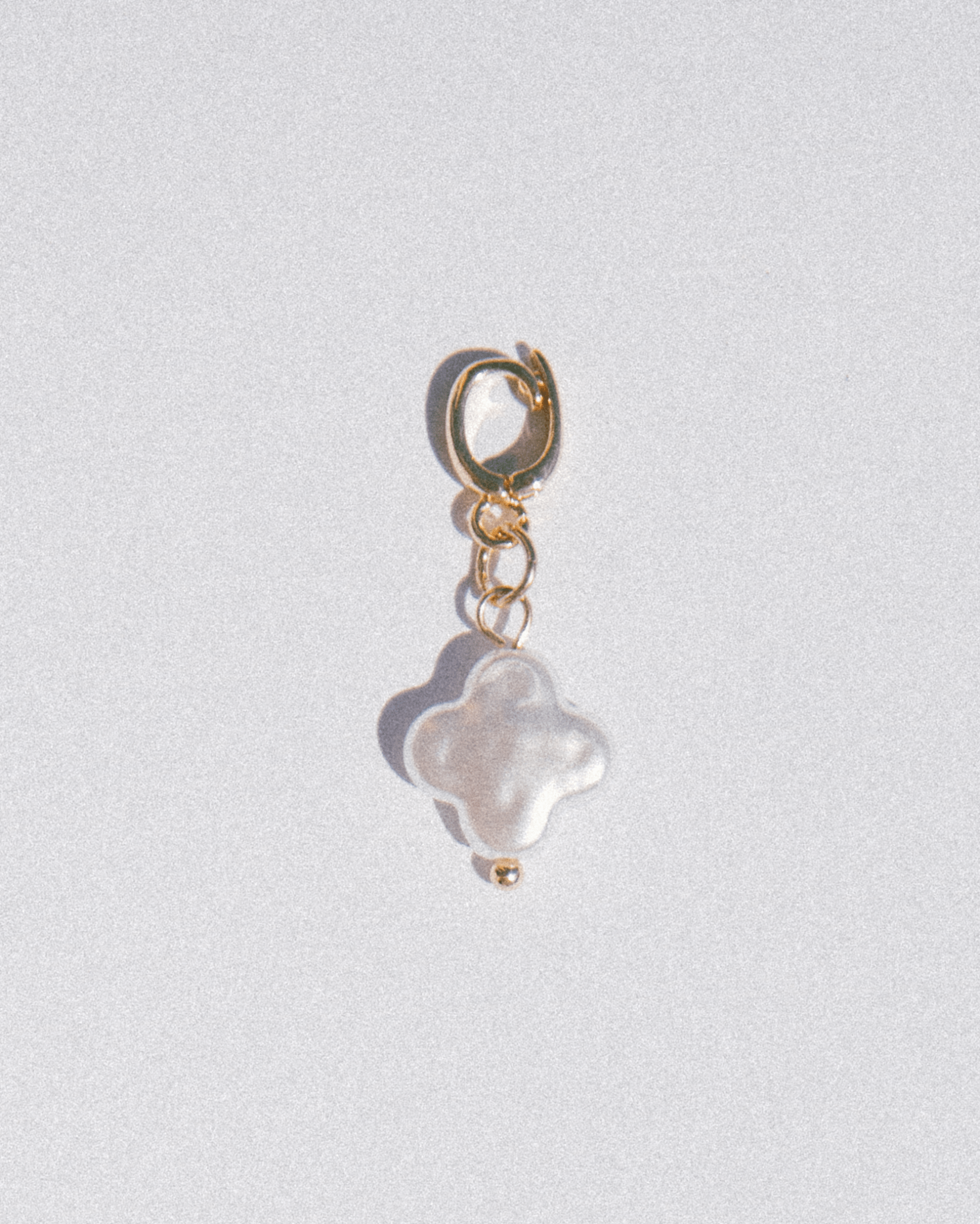 Gold charm with a white pearl on a light gray background