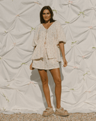 Woman wearing a light-colored outfit against a textured white background