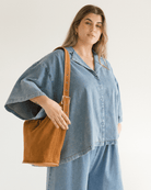 Woman wearing a blue denim outfit holding a brown leather bag against a white background