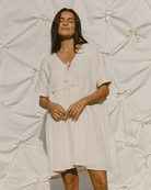 Woman wearing a light-colored dress standing against a textured white background