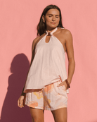 Woman wearing a pink halter top and floral shorts against a pink background