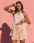 Woman wearing light pink halter top with brown bead and light pink floral flowy shorts with elastic adjustable waist band.