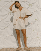 Woman wearing oversized and flowy cream top & shorts set with delicate pink flowers. 