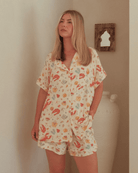 Woman wearing a Australian Christmas inspired patterned pajama set in a room with a neutral wall.