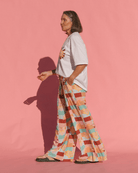 Person wearing a light-colored t-shirt and patterned pants on a pink background