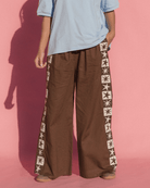 Person wearing brown wide-leg pants with star patterns on a pink background