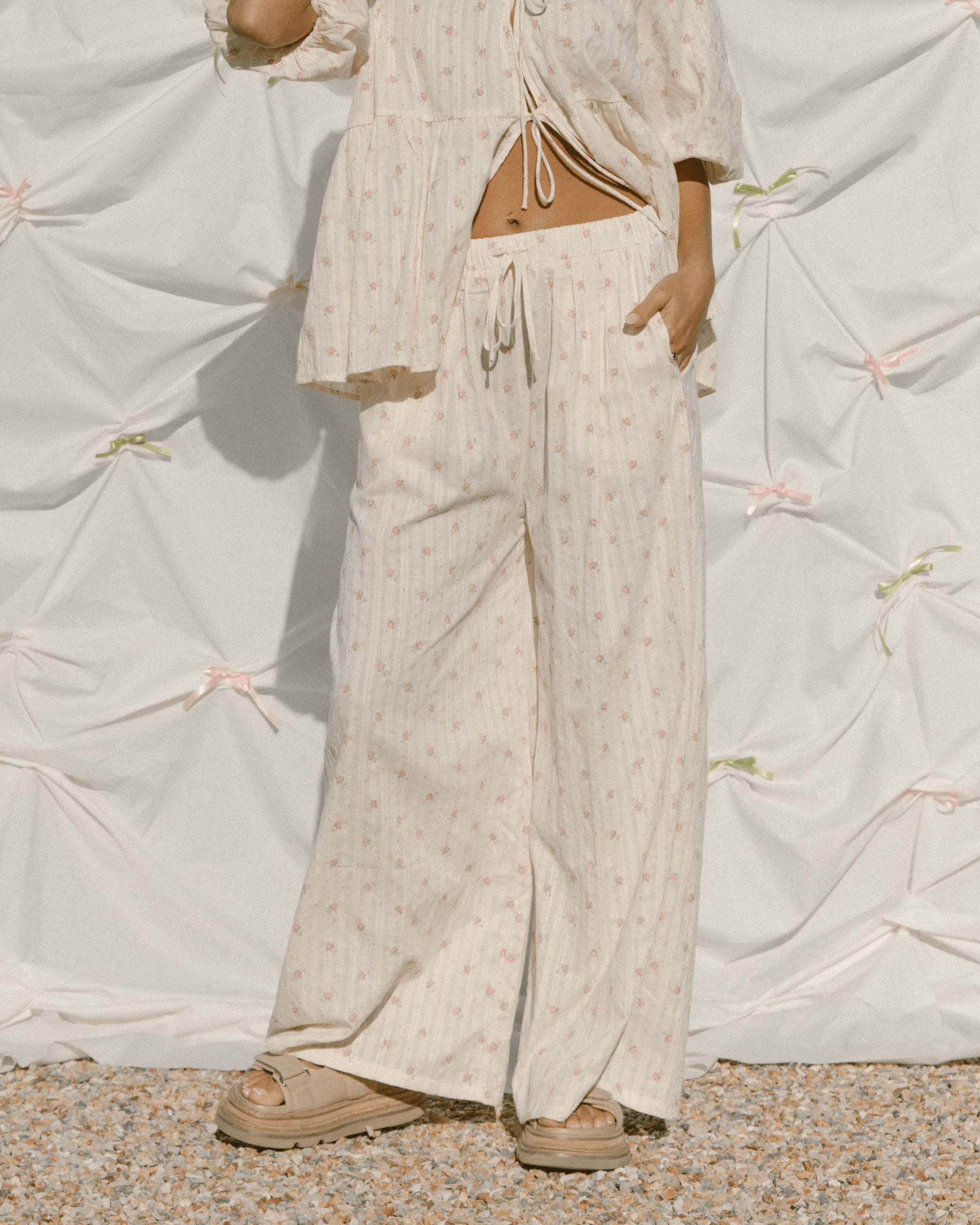 Woman wearing high-waisted wide legged pants in a cream and pink floral pattern. 
