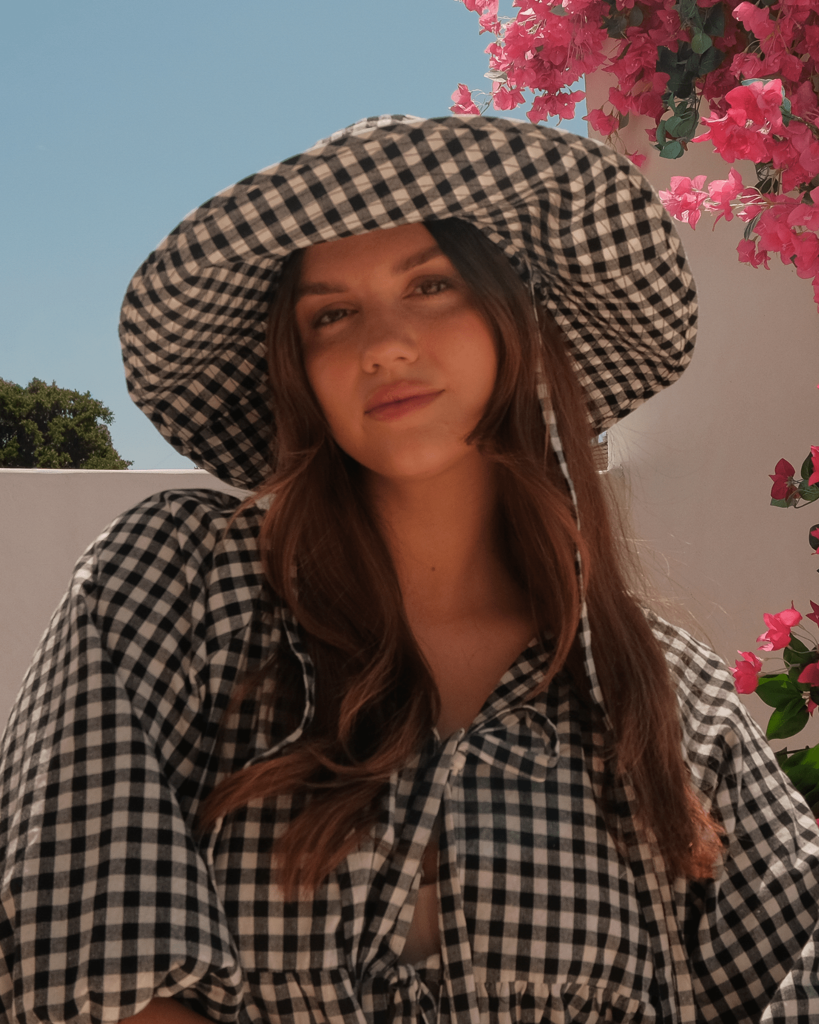 Woman wearing a checkered hat and dress with pink flowers in the background