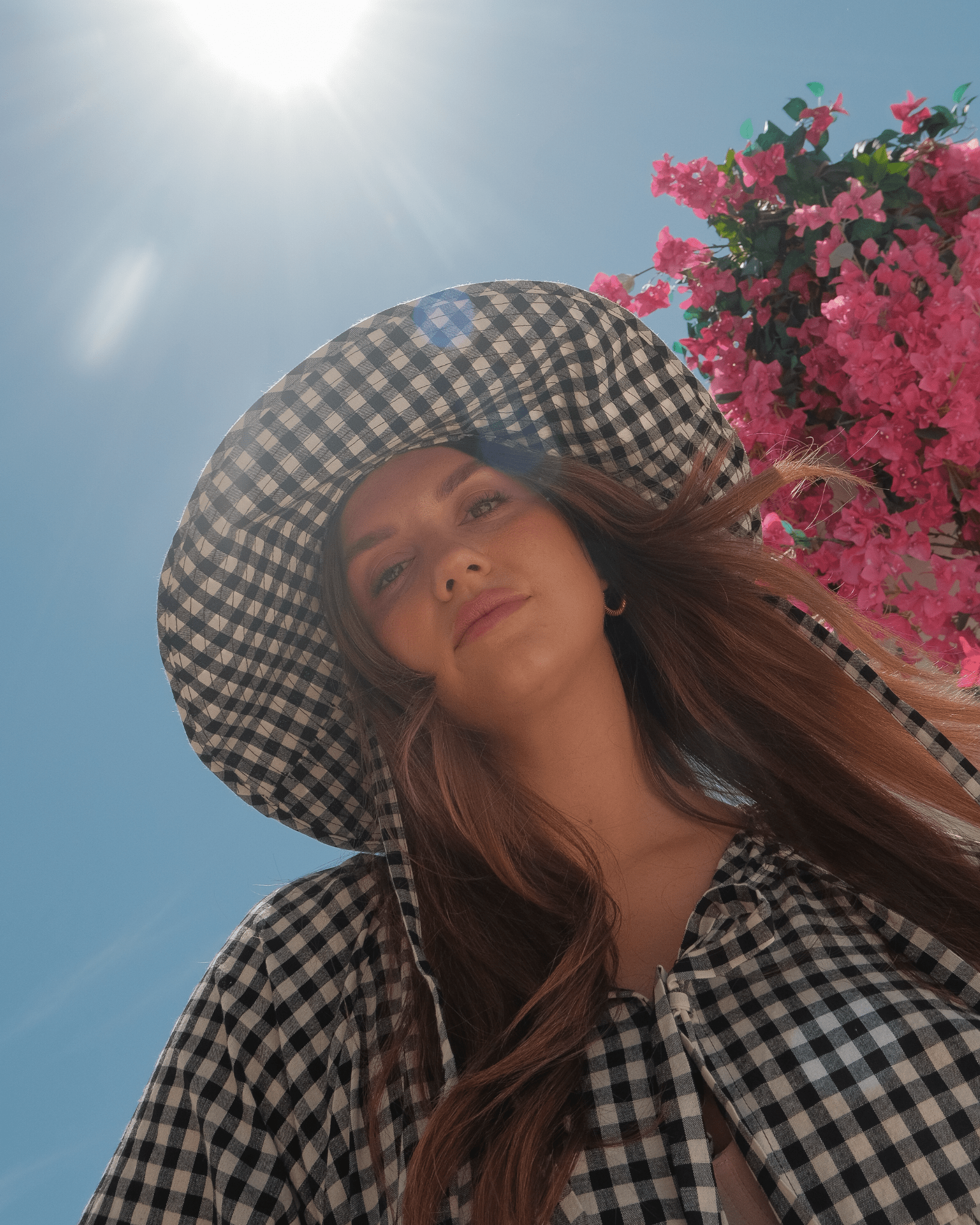 Woman wearing a checkered hat and shirt with pink flowers and blue sky in the background