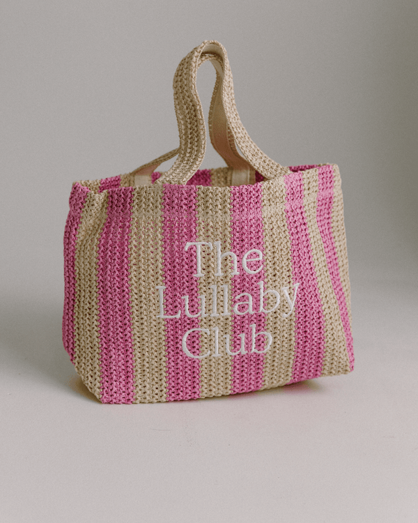 A striped pink and beige raffia tote bag with 'The Lullaby Club' embroidered on it.