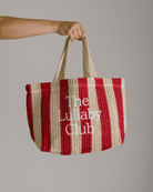 Women holding a woven red and beige striped tote bag with 'The Lullaby Club' embroidered on the front. 