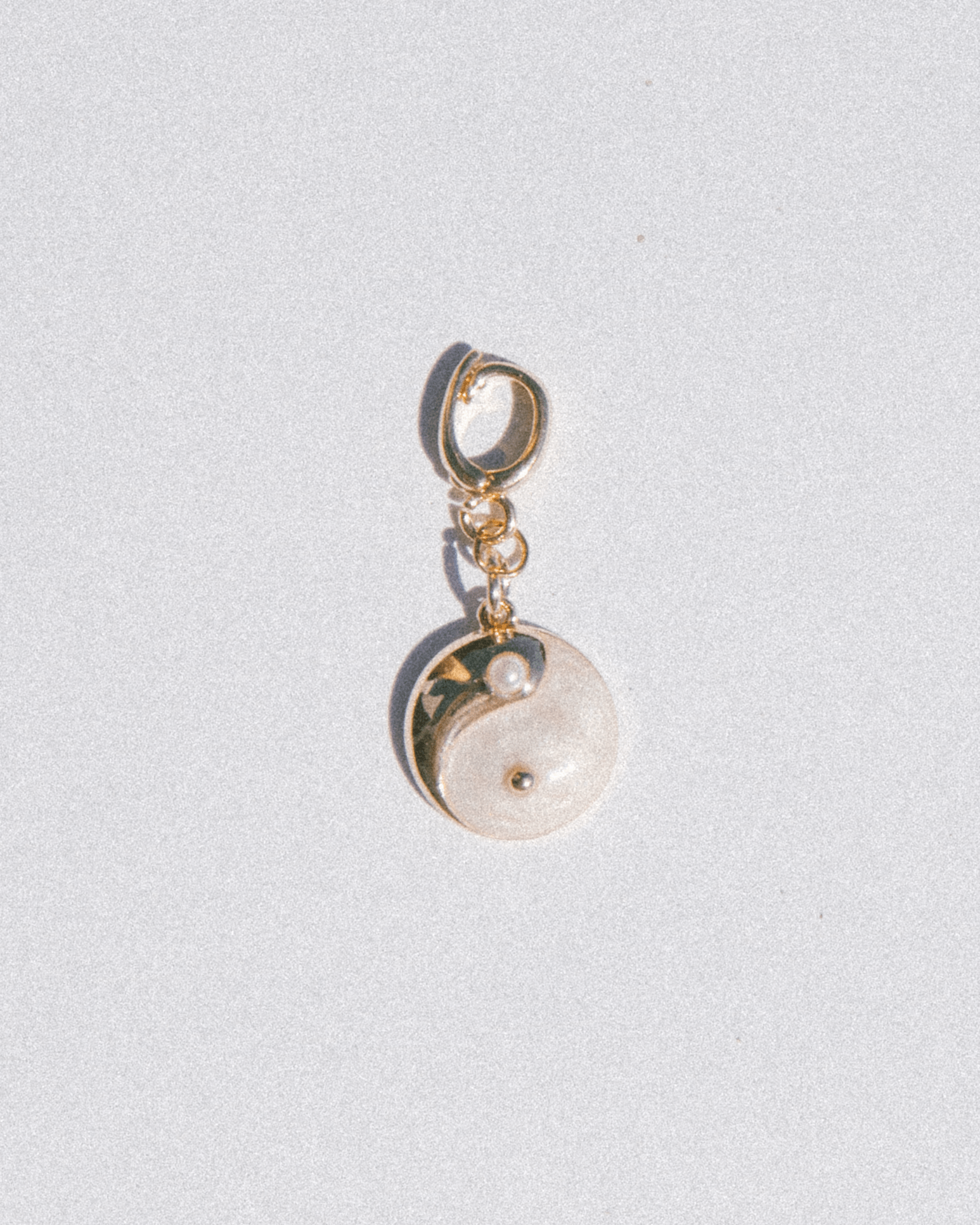 Yin yang charm with gold & pearl accents on a light gray background