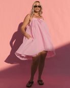 Women wearing a flowy pink summer sleeveless dress with her hands in the side pockets. 