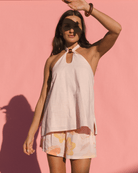 Woman wearing linen/cotton blend flowy pale pink halter top with brown bead and matching floral light pink shorts.